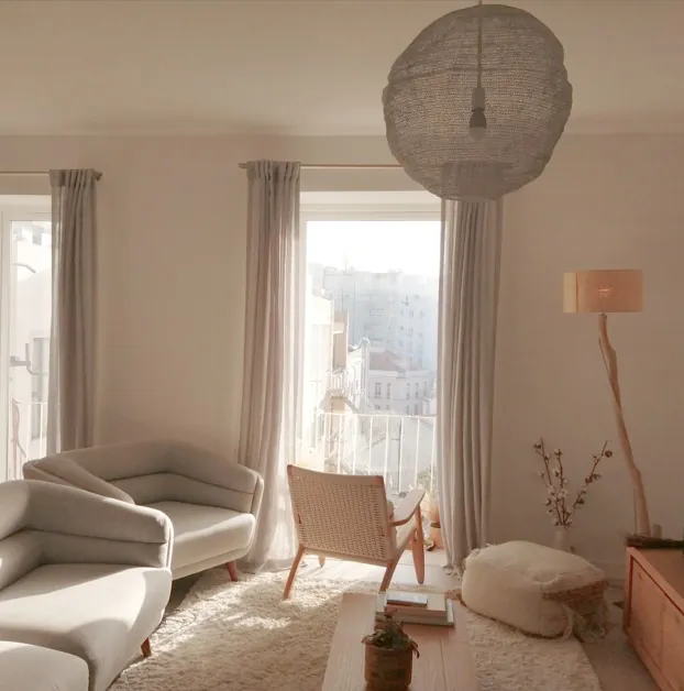 Sunlit living room of a residential apartment in Lisbon with floor-to-ceiling balcony windows.